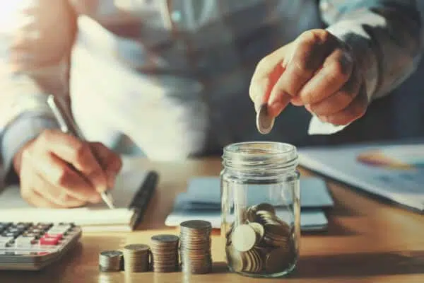 man sitting at a desk. He notes something on a notepad and puts coins on a glass. You also see a calculator and other documents for refinancing