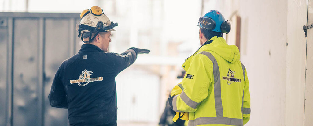 2 menn i arbeidstøy med logoen til saneringsgruppen på ryggen