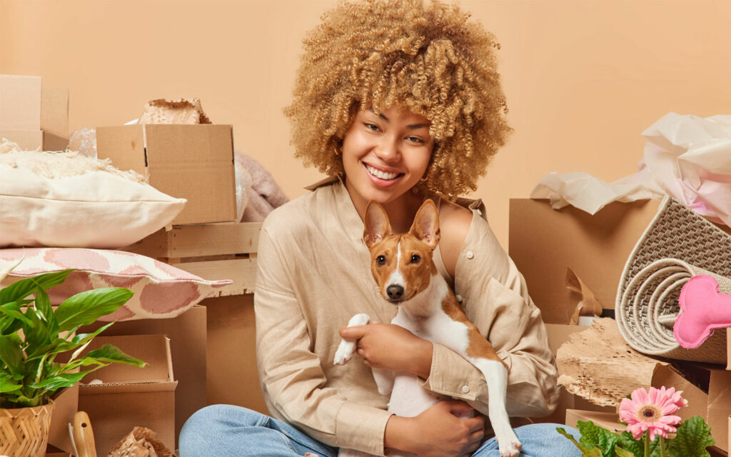 girl with curly hair sits among moving boxes and interiors with a dog on her lap